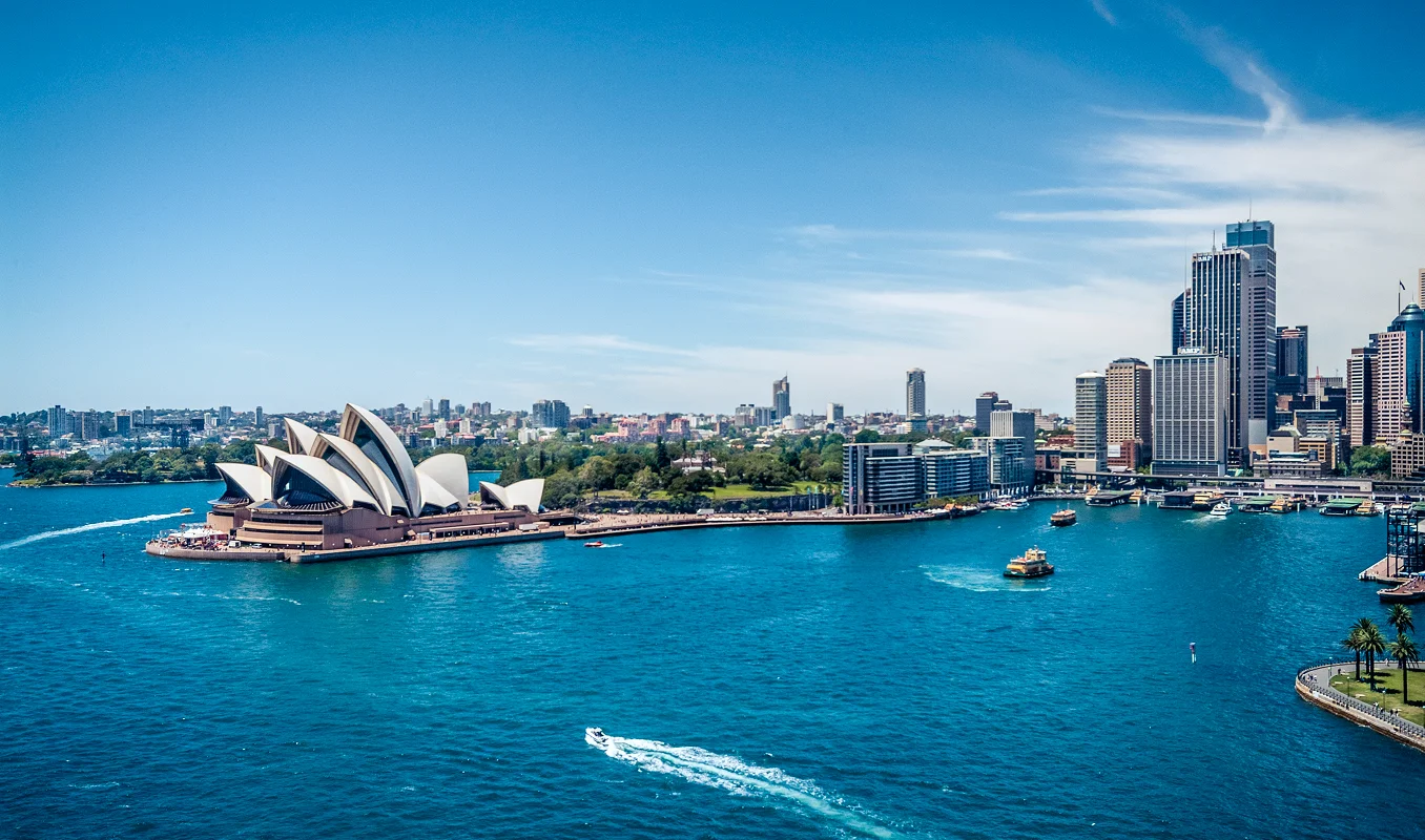 Sydney Harbour with Opera House and city skyline on sunny day with blue water and ferry boats