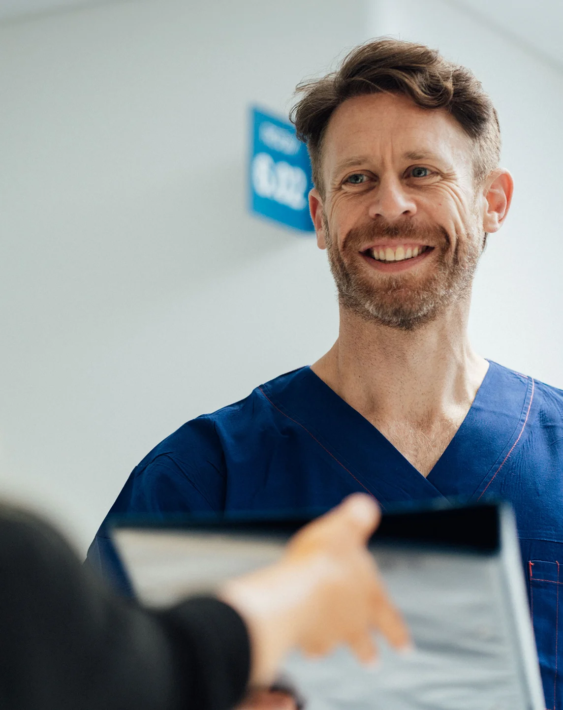 Dr Anthony Barker in blue scrubs consulting with patient in medical office - in New South Wales, Australia