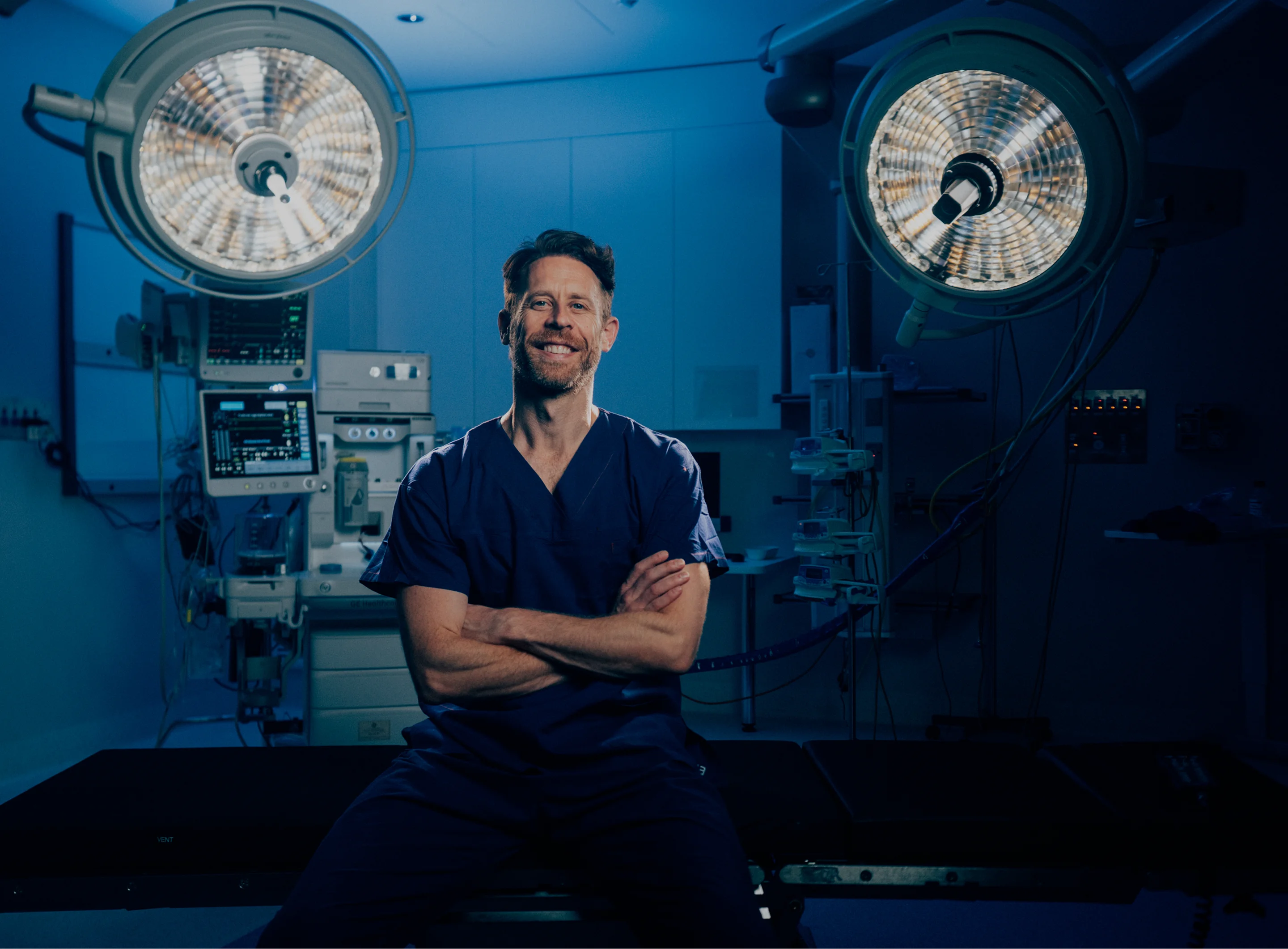 Dr Anthony Barker standing in operating room with surgical lights and medical equipment in background - in New South Wales, Australia